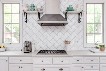 A kitchen detail with shelves on white herringbone tile backsplash, white cabinets, and stainless...