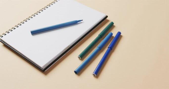 Close up of blue markers with notebook on beige background, in slow motion
