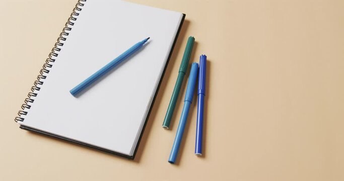 Close up of blue markers with notebook with copy space on beige background, in slow motion