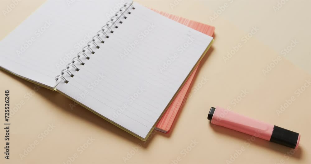 Poster Close up of open notebook with pink marker on beige background, in slow motion