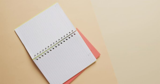 Overhead view of open notebook with pink marker with copy space on beige background, in slow motion