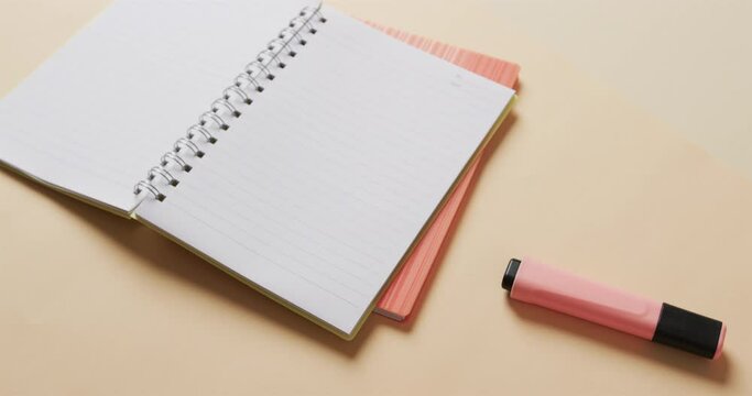 Close up of open notebook with pink marker on beige background, in slow motion
