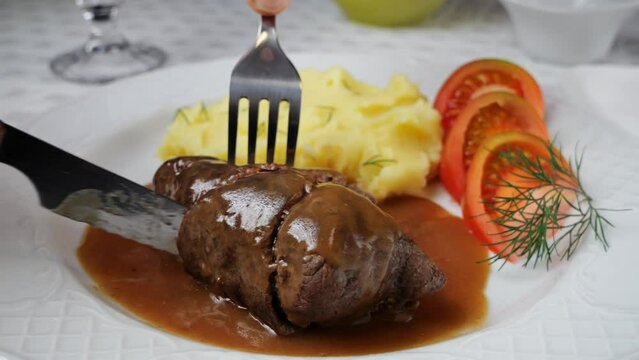 Chef hand cuts with knife beef rouladen stuffed with mustard, onions, pickled cucumber and bacon.
