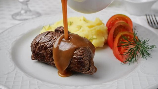 Chef hand pouring brown sauce on beef rouladen stuffed with mustard, onions, pickled cucumber and bacon. Slow motion