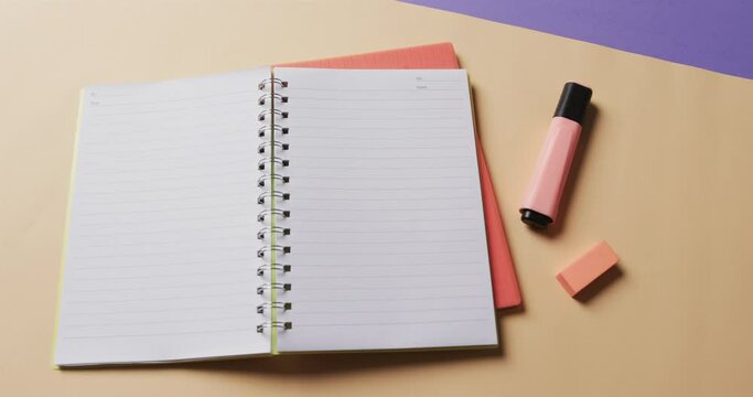 Overhead view of open notebook with school stationery on beige and blue background, in slow motion