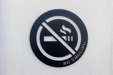 Black steel Non Smoking on building wall, Iron sign hanging on the white concrete wall, Symbolic of Non Smoking in public area, White grey cement texture, Abstract background.
