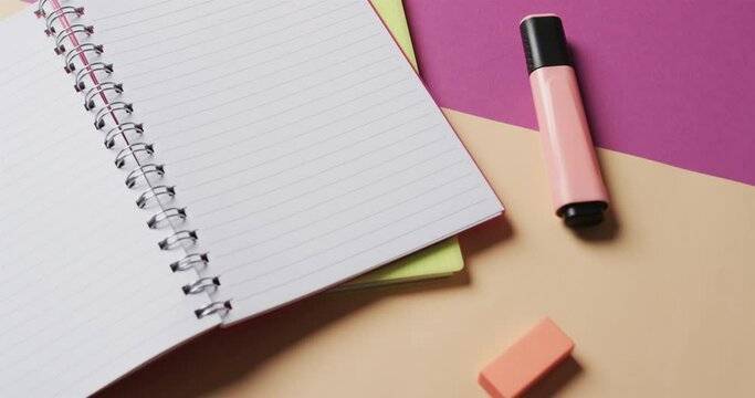 Close up of open notebook with school stationery on beige and purple background, in slow motion