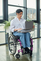 hard working attractive businesswoman with mobility disability in wheelchair looking at laptop