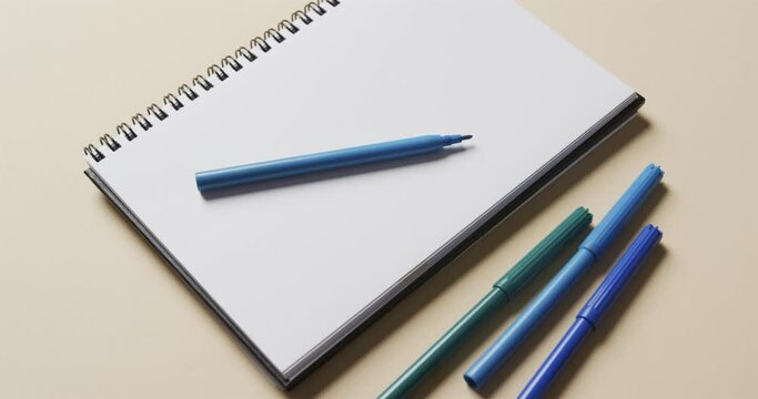 Close up of notebook with blue markers on beige background, in slow motion