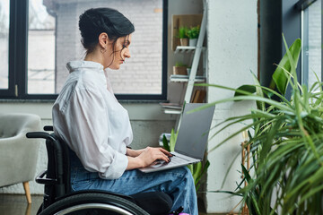 good looking dedicated businesswoman in casual attire in wheelchair holding her laptop in office