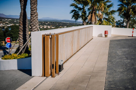Sotogrante, Spain - January 25, 2024 -  a sidewalk with a wooden gate, white walls, palm trees, and a clear sky.