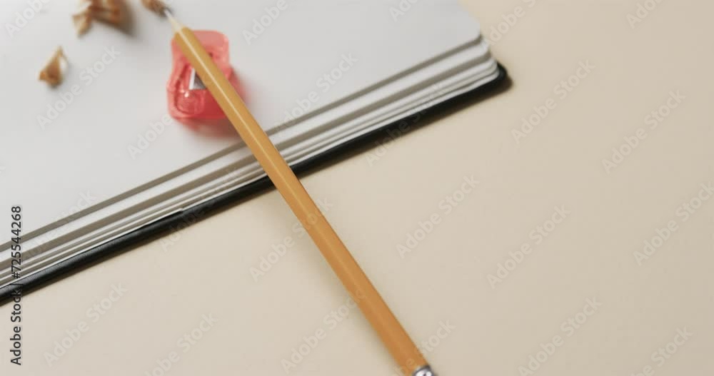 Wall mural Close up of open notebook with pencil and pencil sharpener on beige background, in slow motion