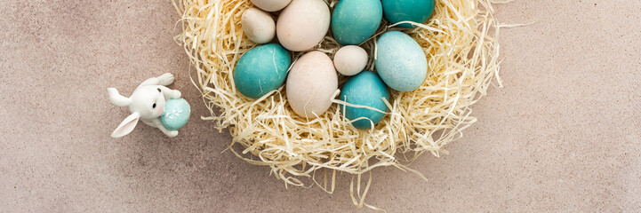 Colorful Easter eggs in a nest and cute bunnies on a pastel pink background, top view, copy space, Easter banner
