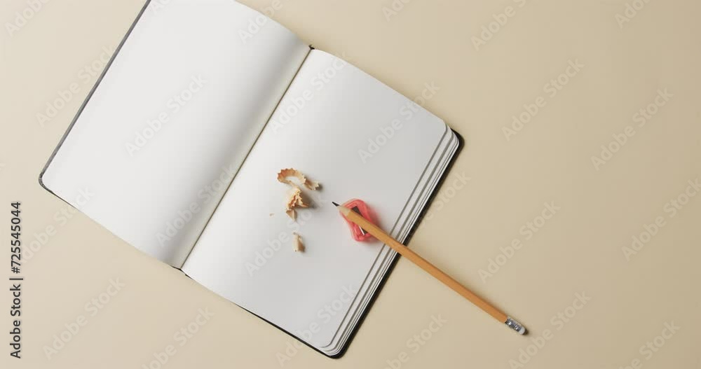 Aufkleber overhead view of open notebook with pencil and pencil sharpener on beige background, in slow motion
