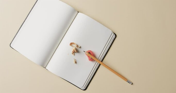 Overhead view of open notebook with pencil and pencil sharpener on beige background, in slow motion
