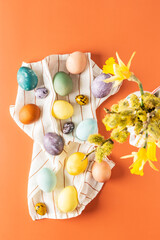 Top view of napkin with dyed natural dyes Easter eggs, bouquet with yellow daffodils in vase on orange background