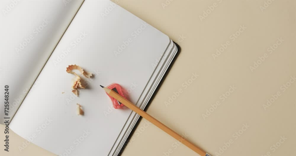 Poster overhead view of open notebook with pencil and pencil sharpener on beige background, in slow motion