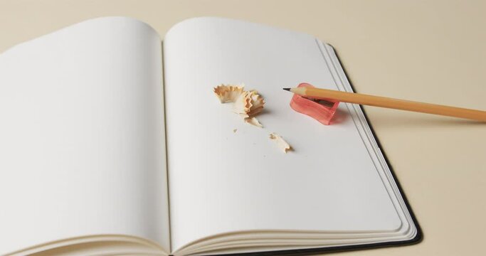 Close up of open notebook with pencil and pencil sharpener on beige background, in slow motion