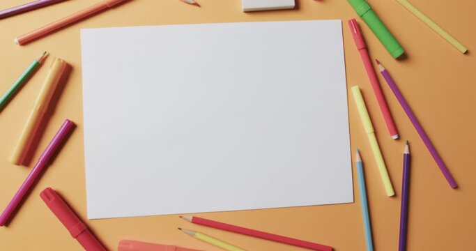 Overhead view of blank sheet of paper with school stationery on beige background, in slow motion