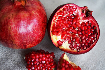A cut pomegranate next to a whole one on a gray background