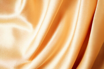 Close-up of yellow silk satin, draped fabric, gold color, elegant background. Beautiful wavy area...
