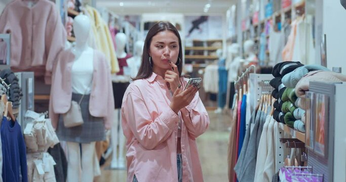 Woman in clothing store texting phone radiates joy combining shopping technology Joy modern living finding perfect outfits. Shopping brings joy symbolizes prosperity Tech-savvy elegance.