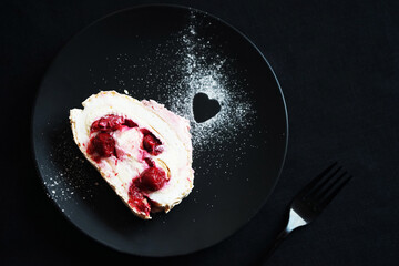 Piece of meringue roll on a black plate on a dark background