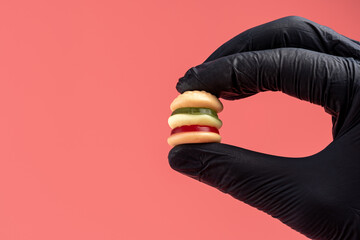 Colorful candy hamburger with a hand in black glove. Minimal food concept.