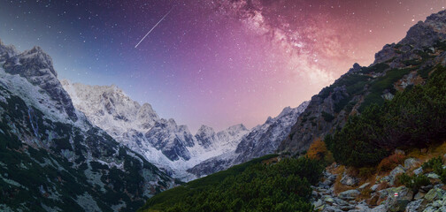 Snow-capped mountain peaks under starry night sky with visible Milky Way and shooting star.