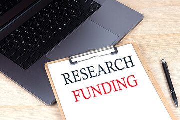 RESEARCH FUNDING text written on a paper clipboard on laptop