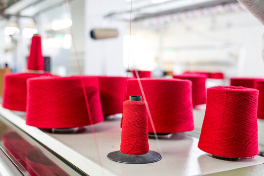 Red yarn spools and thread cones lined up on an automated knitting machine in a textile factory.