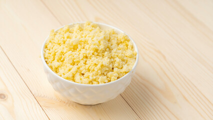 Millet porridge in white cup on wooden background, selective focus