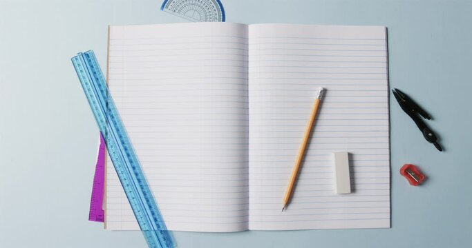 Overhead view of open notebook with school stationery on blue background, in slow motion