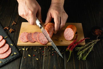 Cooking a hearty breakfast with smoked sausage by the hands of a cook on the kitchen table. Cutting...