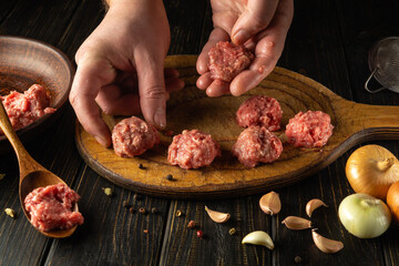 The cook hand places a raw meat cutlet on the kitchen board. Cooking meat on the kitchen table for...