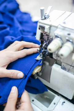 Closeup of tailor hands sewing blue fabric with an industrial overlock machine.