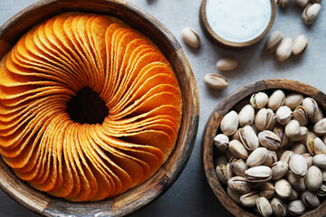 Potato chips and pistachios in wooden bowls next to sauce on gray background