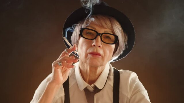Adult woman in gangster style confidently smoking a cigarette in a dark room with subdued lighting, wearing a black hat and glasses, suspenders and a necktie. Camera 8K RAW. 
