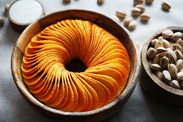 Potato chips and pistachios in wooden bowls next to sauce on gray background