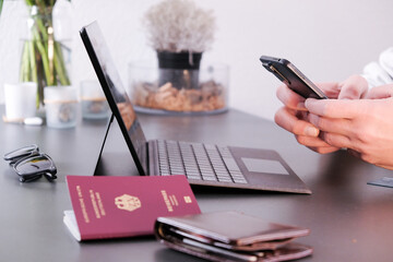 Hands typing on phone with a laptop, German passport and wallet in frame
