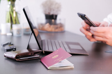 Hands typing on phone with a laptop, German passport and wallet in frame
