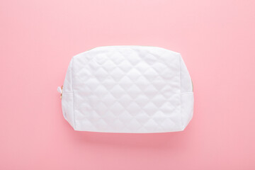 New white female cosmetic travel bag on light pink table background. Pastel color. Closeup. Top...