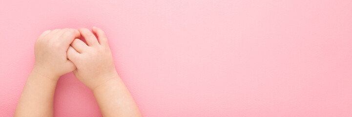 Baby girl hands on light pink table background. Pastel color. Closeup. Point of view shot. Empty...