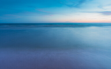 The sea is calm. The sand and water surfaces are smooth. There are no people. blurred motion