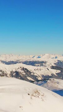 Aerial helicopter shot of calm rural mountain landscape, snow-covered mountain peaks and ski resort landscape at the Austrian Alps on a sunny afternoon day. vertical video