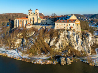 Fototapeta na wymiar Tyniec near Krakow, Poland. Benedictine abbey, monastery and church on the steep rocky rocky cliff and Vistula river. Aerial view at sunset in winter with snow and trees