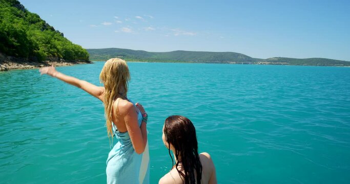 Women, friends and ocean or wave on beach or swimming vacation on tropical island for summer, adventure or travel. Female people, hand gesture and towel by water for holiday relax, paradise or hello