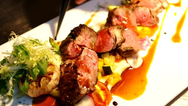 chief plating dot on sliced dry-aged steak with sauce garnish grilled garlic bulb on mashed potato salad raw video