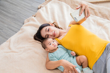 Selective focus of Asian young mother kissing baby on bed, Beautiful woman hugging toddler infant lying down together on soft fur. Cute newborn child playing with mom. family motherhood health care