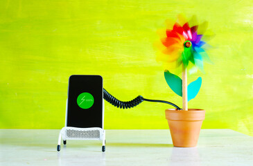 Charging mobile devices with green sustainable energy, smartphone and toy wind turbine, conceptual...
